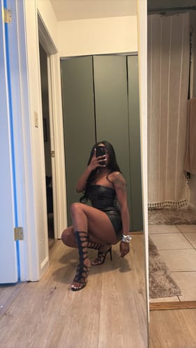 Customer squatting in a mirror, showing off the tall, black lace-up Snake Heels.