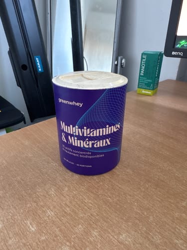 Un client montre le pot bleu des Multivitamines & Minéraux posé sur un bureau.