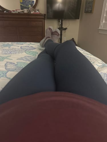 Close-up of a reviewer lounging on a bed wearing the Deep Navy Piper Pocket Leggings.