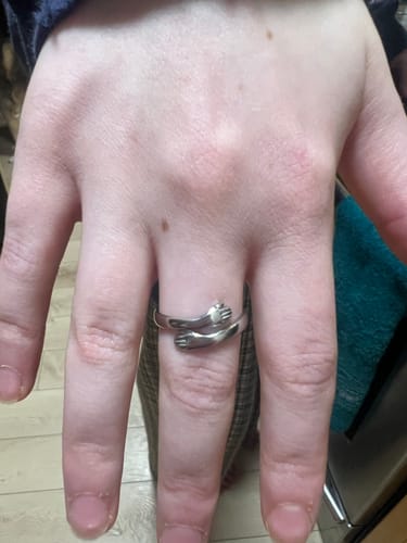Customer's hand wearing the silver Hug From Heaven Ring, designed as a pair of arms embracing the finger.