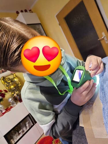 Rezensent zeigt ein Kind, das das grüne Abenteuer-Mikroskop mit dem Trageband um den Hals hält und es benutzt.