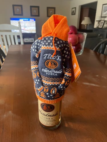 Reviewer's photo of a Tito's Vodka bottle wearing a small knitted hoodie, sitting on a table.