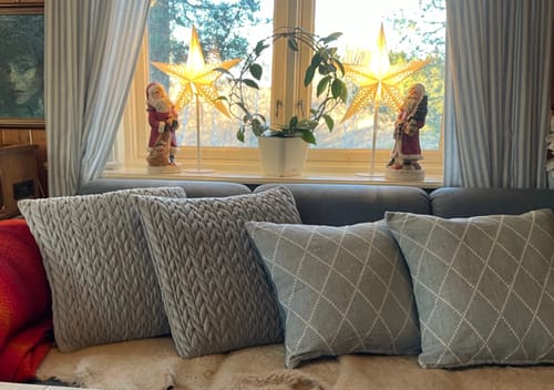 Kundens to jaquard putetrekk i aqua vist på en sofa sammen med to andre flettede puter.