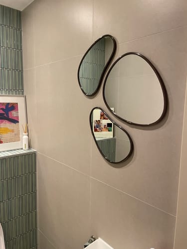 Recensent toont de set van drie Umbra Hubba Pebble spiegels gemonteerd op een lichte tegelwand.