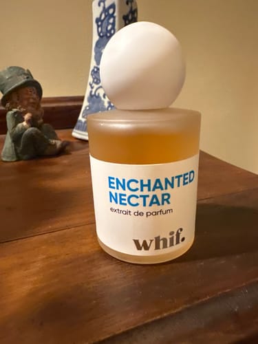 Customer's bottle of Enchanted Nectar perfume in its frosted glass bottle with a round white cap, sitting on a wooden surface.