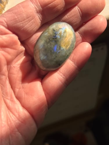 Reviewer's hand holding a smooth, oval labradorite crystal with blue and gold flashes.
