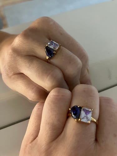 Reviewer's Toi Et Moi Birthstone Ring with blue and purple stones, shown on a hand and its reflection.