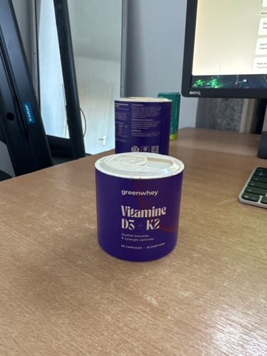 Client montrant le pot violet de Vitamine D3 + K2 posé sur un bureau.