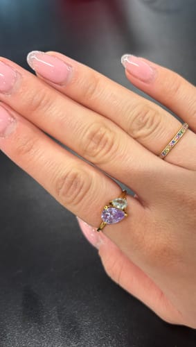 Reviewer wearing the dainty Leesha Birthstone Ring with its purple and light blue pear-cut stones on a gold band.