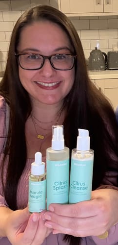 Customer smiling while holding three products from the 5-Step Clear Skin Kit in her hands.