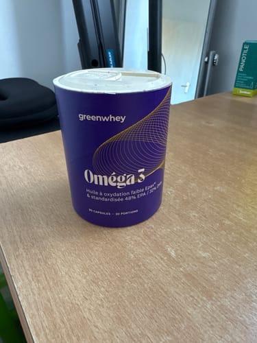 Un client montre son pot d'Oméga 3 EPAX® violet et cylindrique, posé sur un bureau en bois.