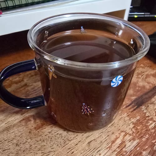 Customer's ready-to-drink EssenceQi soup served in a clear glass mug on a wooden surface.