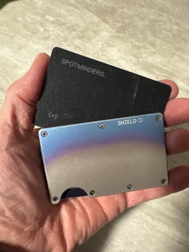 Customer holding the black SPOTMINDERS Tracking Card in their hand next to a metal wallet.