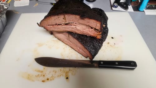 Customer's cooked USDA Prime Brisket cut in half on a cutting board, revealing the juicy interior and dark crust.