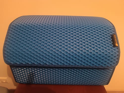 Recenzent pokazuje teksturowany, niebieski organizer do bagażnika z zamkniętą pokrywą.