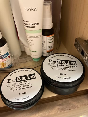 Reviewer's two black F-Balm tins sitting on a wooden shelf among other toiletries.