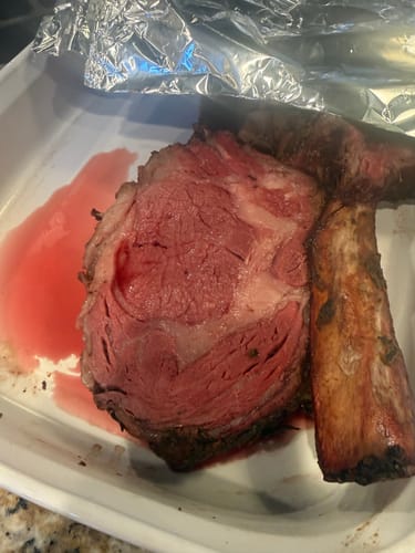 Customer's cooked Tomahawk Prime Rib Roast sliced open in a pan, showing a rare pink center.