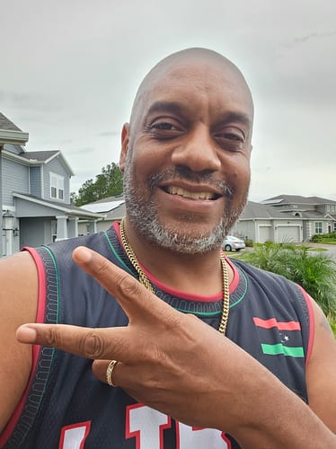 Customer smiling in a selfie while wearing the black Libya Custom Basketball Jersey outdoors.