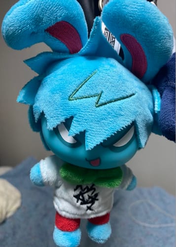 Close-up of a customer's blue Alien Stage Rabbit Series plush charm with spiky hair and a white shirt.