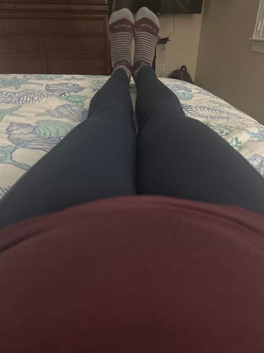Reviewer relaxing on a bed, showing their striped Amelia No Show Socks matching their grape-colored shirt.