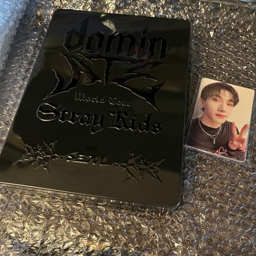 Reviewer's Stray Kids World Tour DVD in a black tin case alongside a photocard.