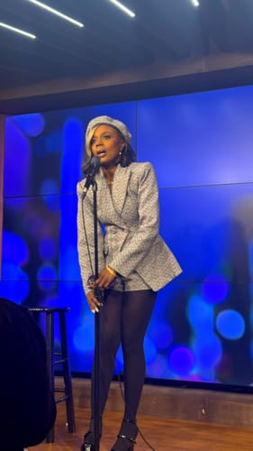 Reviewer on stage wearing the asymmetrical Chevron Power Suit Blazer with a matching beret and black tights.