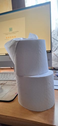 Avis d'un client : deux rouleaux de papier toilette compact empilés sur un bureau devant un ordinateur.