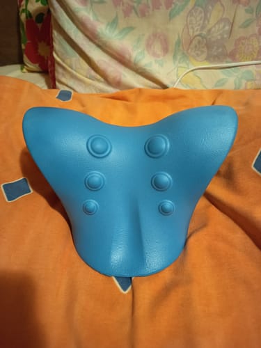 Vásárló kék, masszírozópontos Kiropraktikus Nyak- és Váll Lazító Párnája egy narancssárga takarón.