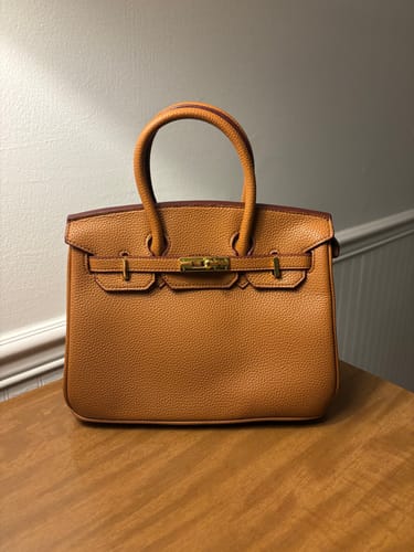 Customer's tan Warkin Bag with a pebbled finish and gold hardware, shown on a wooden table.