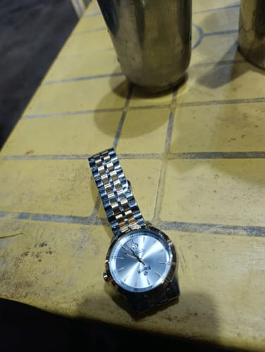 Customer's Stupendous watch with a two-tone band and silver dial, placed on a yellow tiled table.