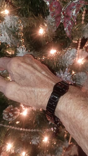 Reviewer wearing the black Valor Cross Magnetic Bracelet on their wrist by a lit Christmas tree.