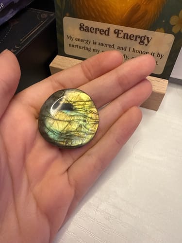 Customer holding a round, iridescent monthly crystal in their palm, showing its beautiful yellow and green colors.