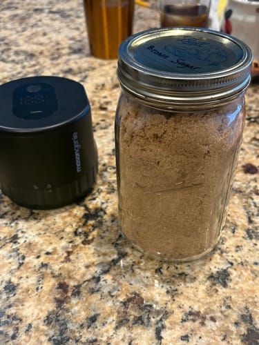 Reviewer's black Mason Genie Vacuum Sealer on a counter next to a sealed mason jar of brown sugar.
