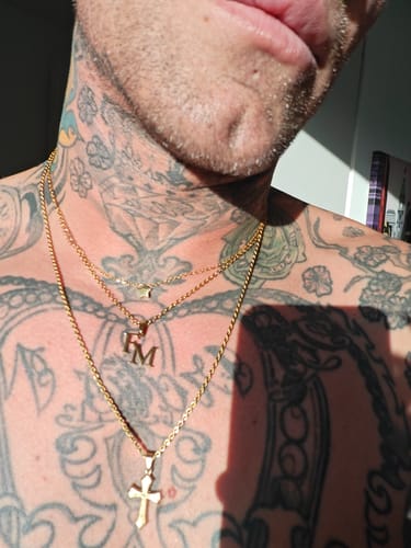 Kunde trägt die goldene Initialen-Kette als Lagenlook über seinen Tattoos auf der Brust.