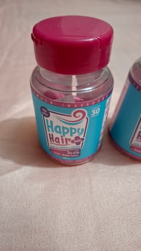 Um cliente mostra um pote do suplemento Happy Hair com o rótulo azul e a tampa rosa.
