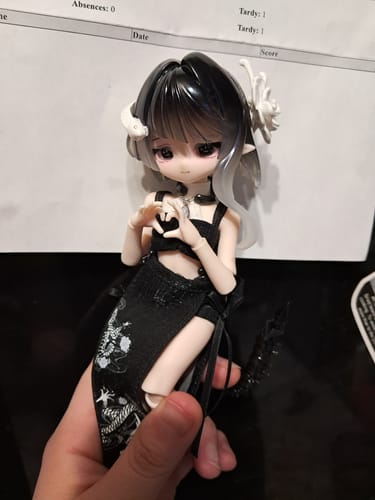 Reviewer holding the Finola action figure. The doll wears a black outfit and makes a heart shape with its hands.