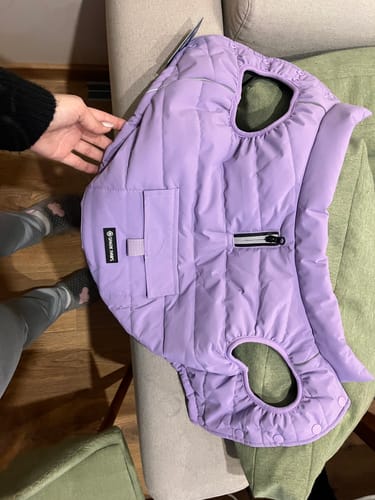 Reviewer holding the lilac WarmShield Jacket, showing the quilted exterior, leash zipper, and pocket.