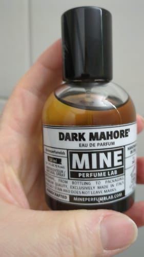 Un recensore tiene in mano la boccetta di profumo DARK MAHORE' in vetro trasparente.