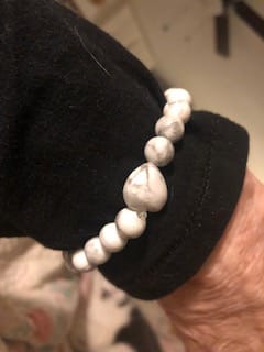 Close-up of a reviewer's arm wearing a white, marbled crystal bracelet with a heart-shaped bead.