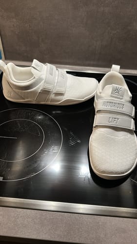 Reviewer's white Notorious Lift Sumo Sole Gen 4 shoes on a black stovetop, showing front and side views.