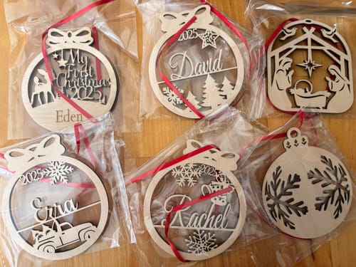 Customer's six personalized wooden Christmas ornaments with different designs, shown in their clear packaging with red ribbons.