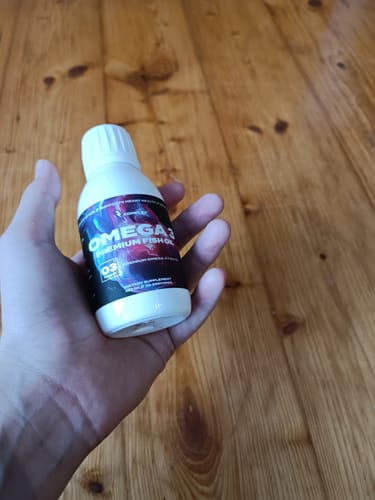 A customer holds the bottle of Complex Omega 3 Premium Fish Oil in their hand over a wooden surface.