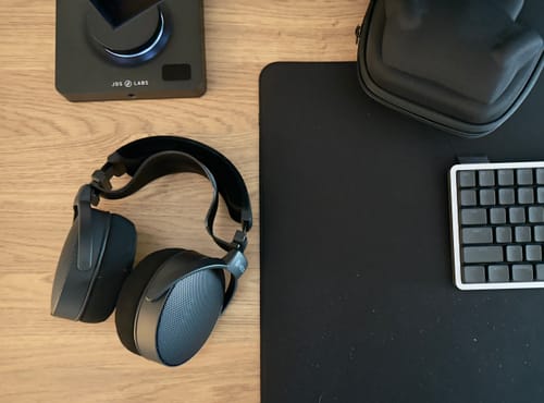 Customer's black HEDD Audio HEDDphone D1 headphones on a wooden desk next to an amplifier and the included carry case.