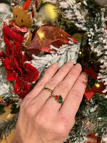 Customer's hand wearing the personalized Leesha Ring with festive green and red stones in front of a Christmas tree.