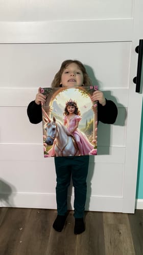 A happy child holding her custom Rose Blossom Unicorn Princess portrait in front of a white door.