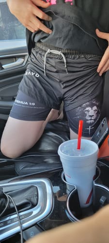 Customer sitting in a car wearing the black Joshua 1:9 'Lion' Girls Performance Shorts, showing the graphic details on the legs.