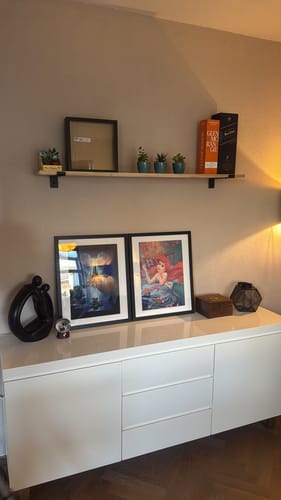 Recensents eiken wandplank met zwarte dragers, gemonteerd aan de muur boven een wit dressoir.