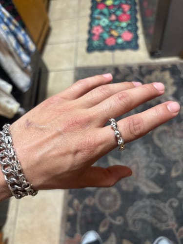 A customer's hand wearing the silver 10 Stages of Addiction Ring and a chain bracelet.