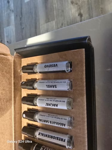 Recensore mostra una vista ravvicinata di alcuni campioni di profumo nel loro cofanetto di cartone.