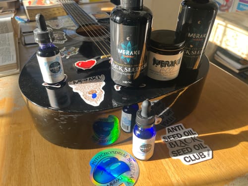Customer's Meraki Blu Methylene Blue bottle on a guitar with other Meraki products and stickers.